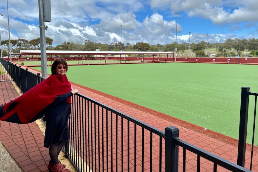 A woman wearing black and red stands in front of a large bowling pitch.