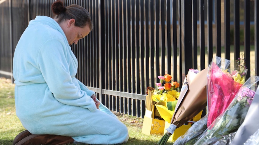 A woman bows her head in front of flowers at the school.