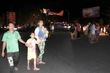 A family with a small child anbd baby walks on a darkened street.
