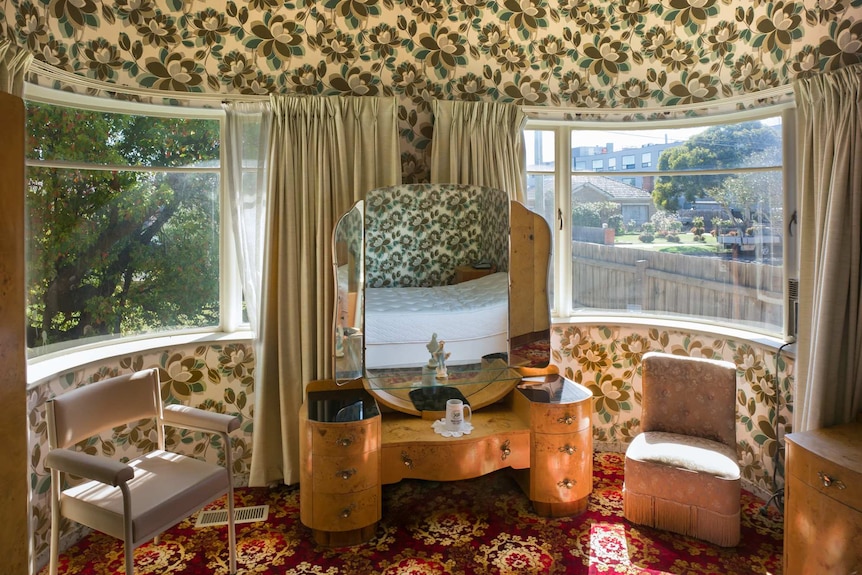 Viewing from inside a bedroom with two large curved windows with bright magnolia-themed wallpaper and red patterned carpet.