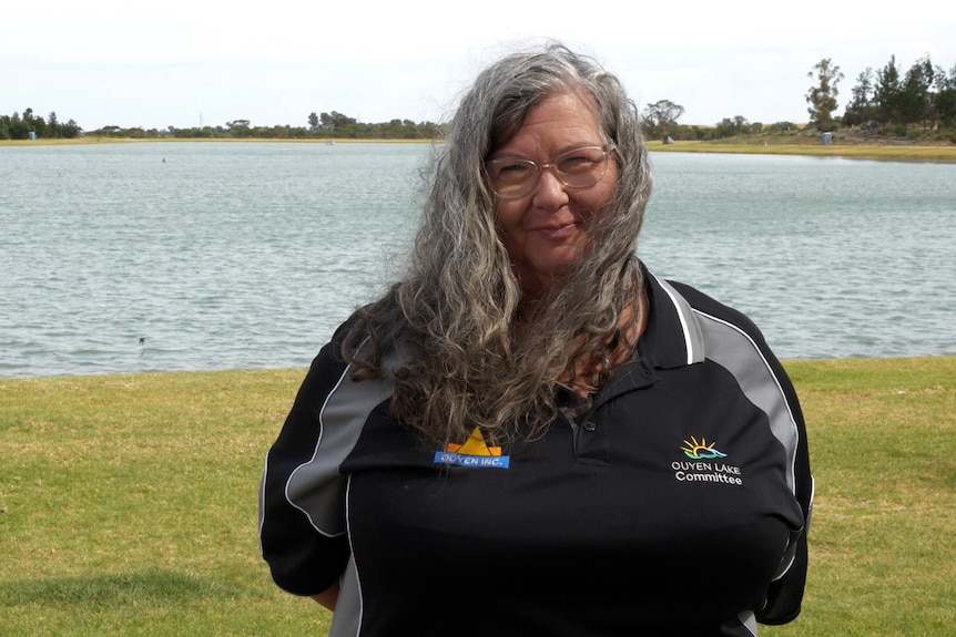 Lady with long wavy hair smiling at camera in front of a lake