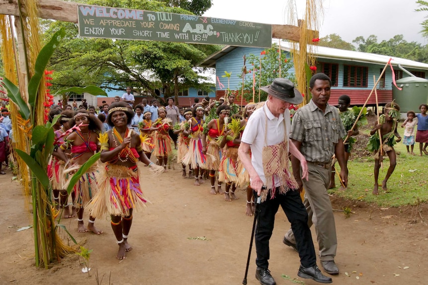 Sean Dorney walks through Tulu under a sign welcoming him and the ABC.