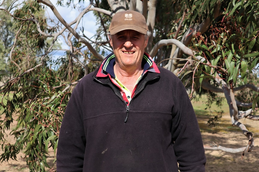 Male farmer standing in front of gumtree smiling.