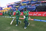 Two batsmen walk out onto the field to open a cricket innings with fans behind them