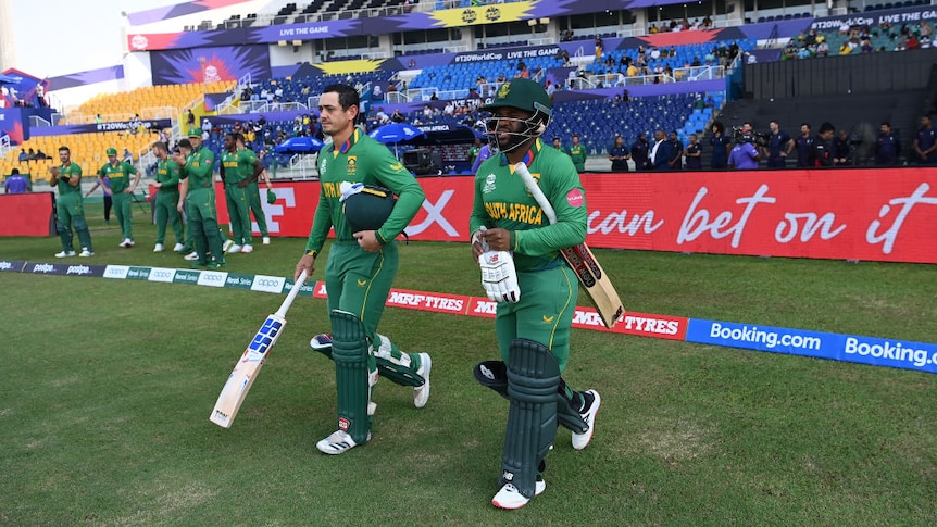 Two batsmen walk out onto the field to open a cricket innings with fans behind them