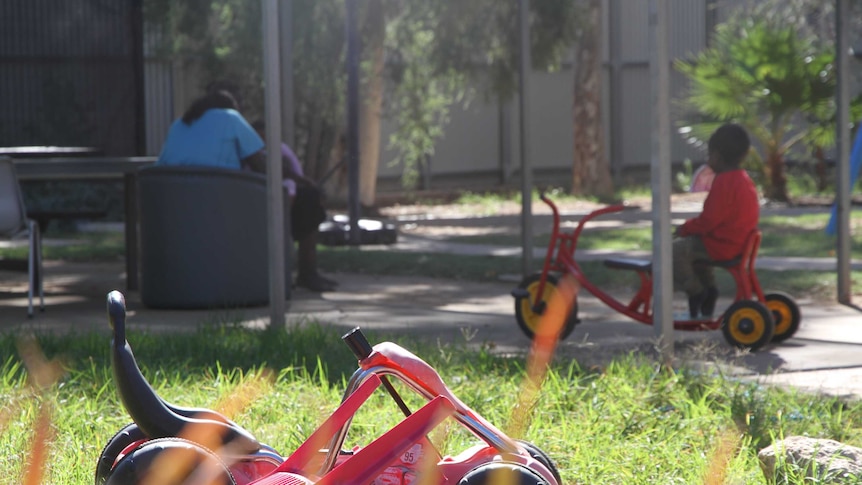 Child plays on tricycle in the distance at an Alice Springs homeless shelter