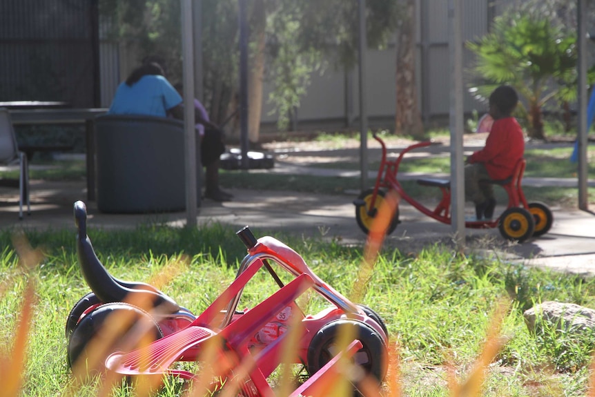 Child plays on tricycle in the distance at an Alice Springs homeless shelter