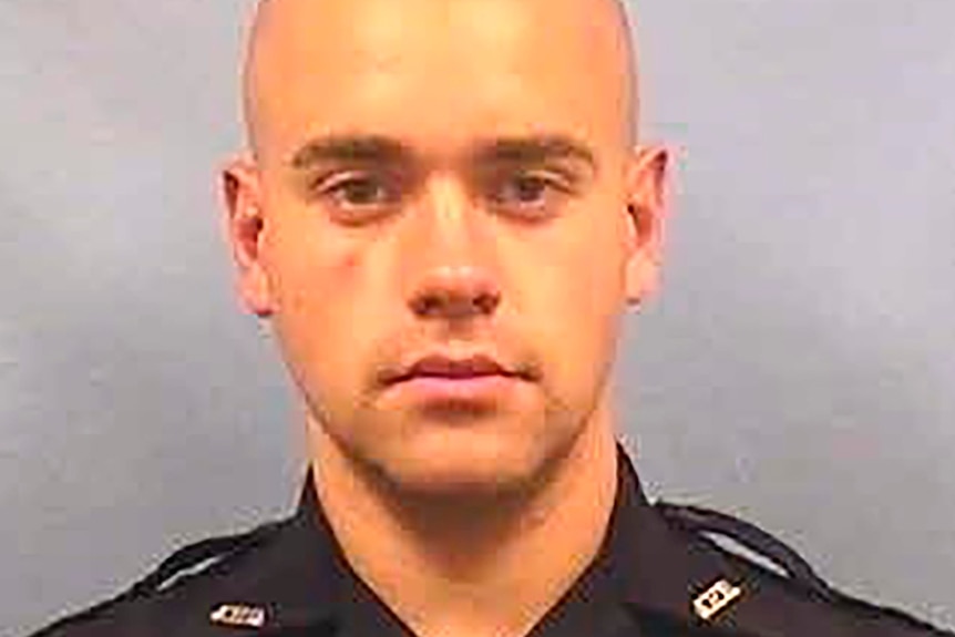 a headshot of a male police officer in uniform with a shaved head