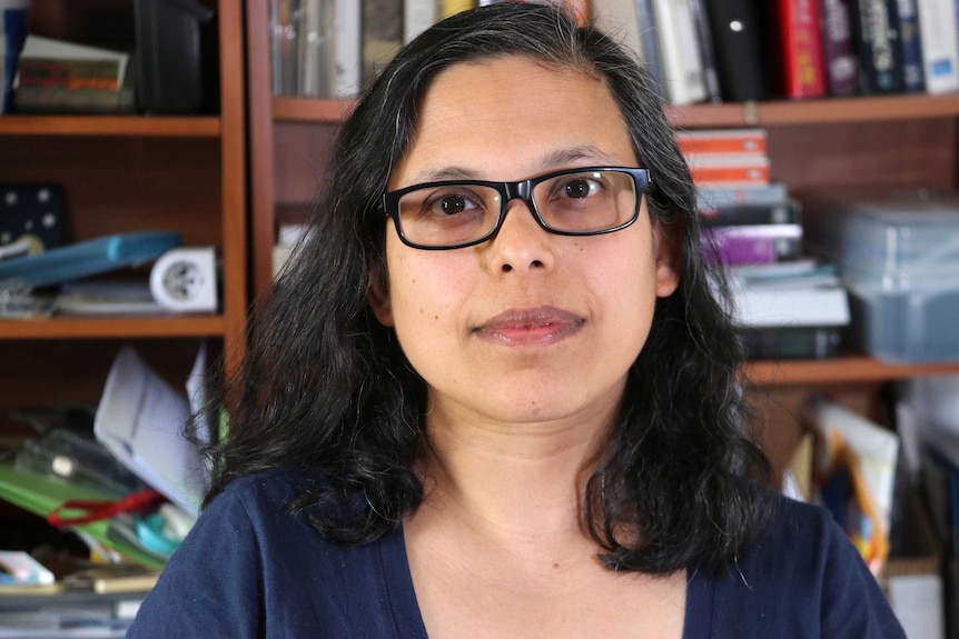 Head shot of a dark-haired woman wearing glasses with a bookshelf behind her.