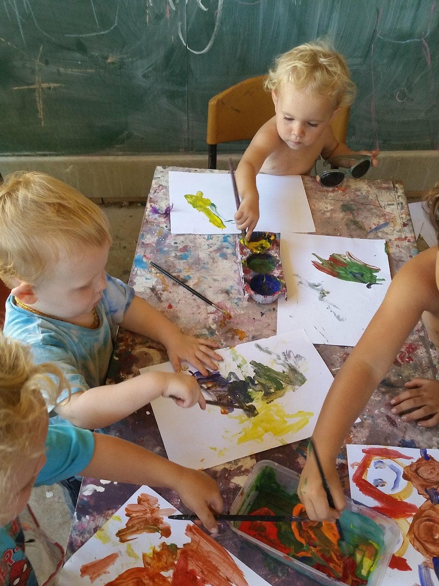 Children sitting around a table painting in a home classroom