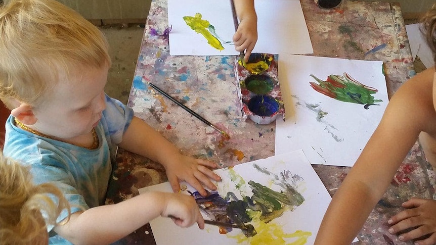 Children sitting around a table painting in a home classroom