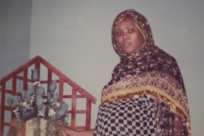 A woman wearing a head scarf standing next to a flower arrangement