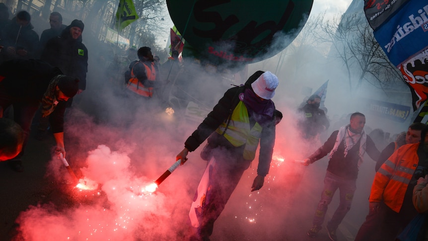 A person holds a red flare as smoke billows.