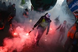 A person holds a red flare as smoke billows.
