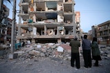 People stand and look at a destroyed building.