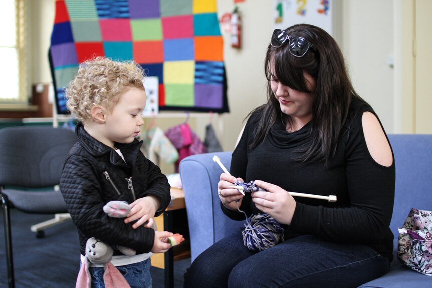 Single mother Chanelle Pilling on the couch showing her daughter Holly how to knit.