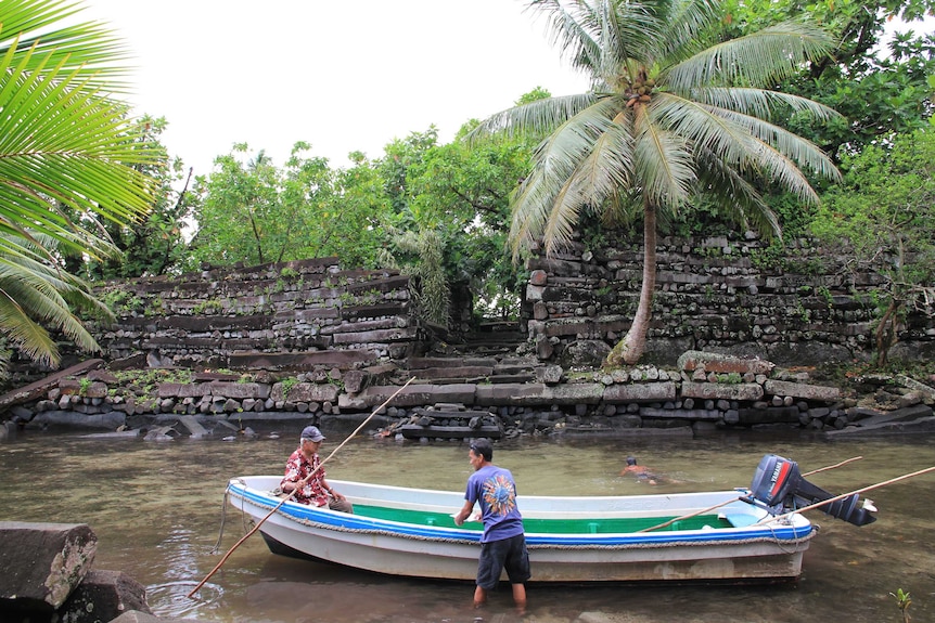 A boat is moored near a stone stairway as locals secure the boat.