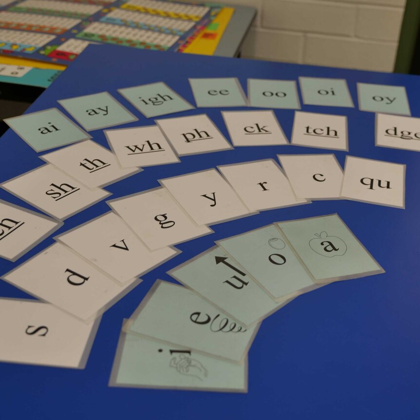 Cards with pictures of letters and vowel sounds, spread across a desk in a classroom.