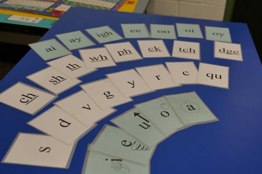 Cards with pictures of letters and vowel sounds, spread across a desk in a classroom.