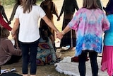 Women hold hands in a ceremony under a pergola.