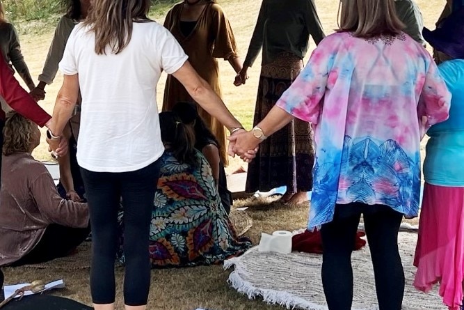Women hold hands in a ceremony under a pergola.