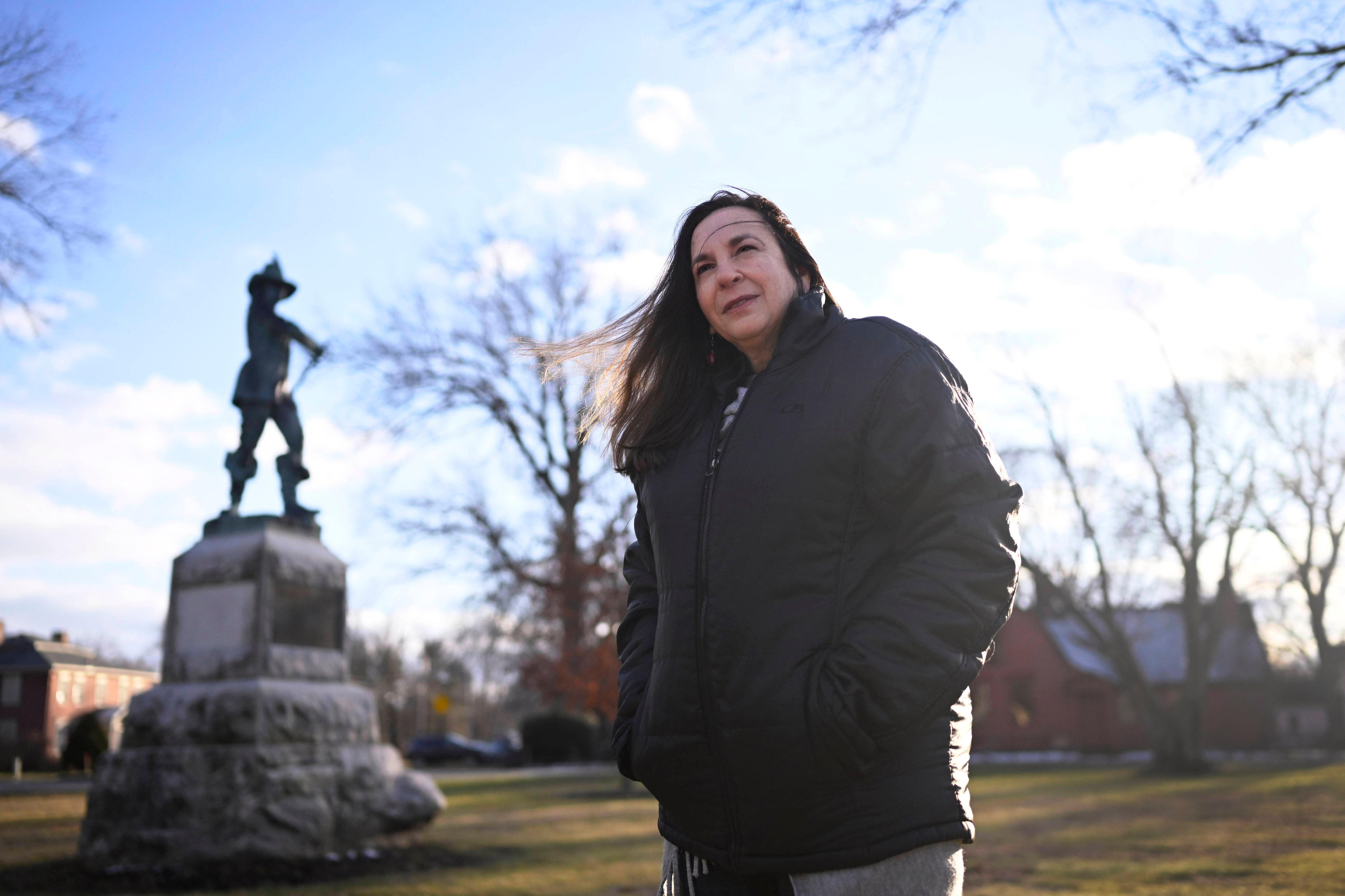 A woman stands in a park with a statue behind her