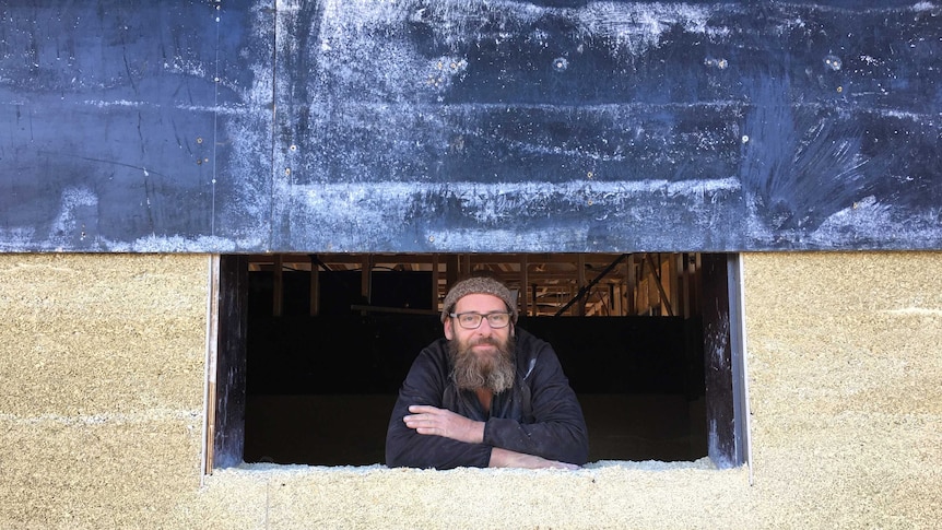 a man leans inside a new window framed by a hempcrete wall