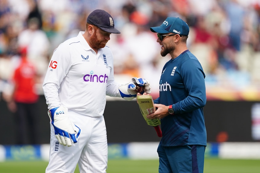 England wicketkeeper Jonny Bairstow speaks to coach Brendon McCullum, who is holding a bat, on the cricket field.