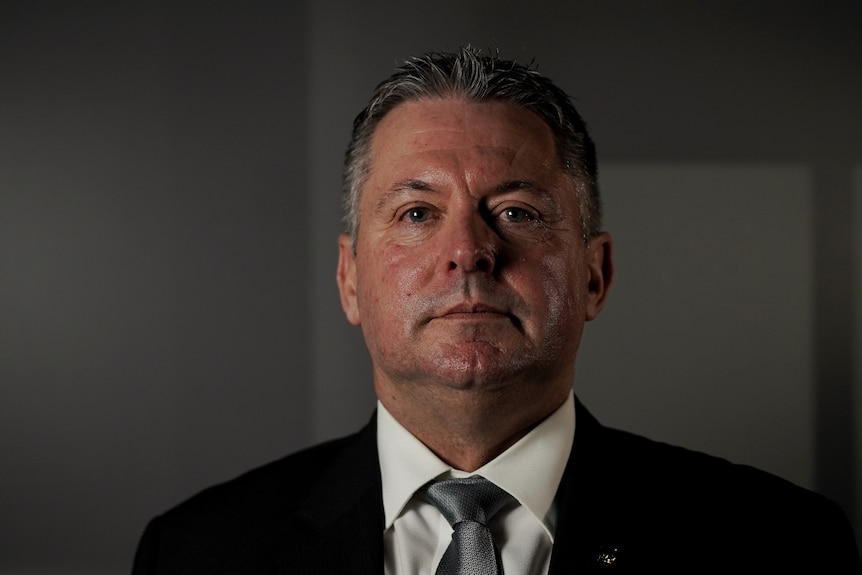 A man in a suit and tie looks into the camera with a serious expression.