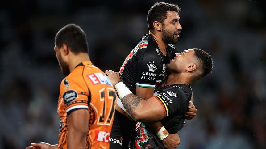 South Sydney Rabbitohs' Alex Johnston is lifted into the air by a teammate after a try. A Tigers player is nearby.