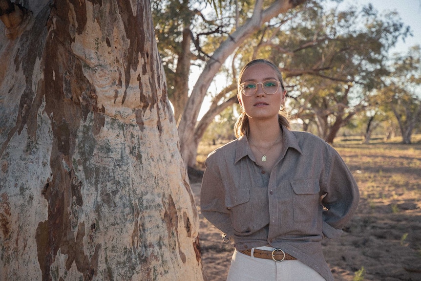 A woman wearing glasses standing next to a big tree