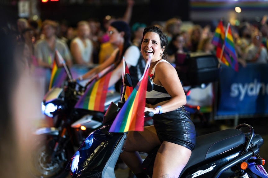 A woman with a rainbow flag sat on a motorbike