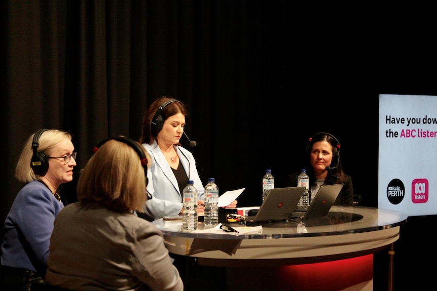 Four women wearing headphones sit at a table with their laptops.