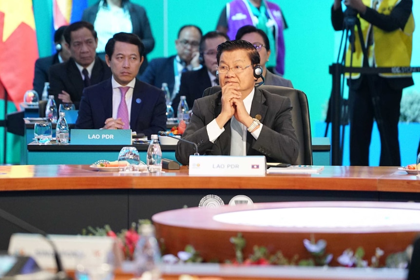 Laos Prime Minister Thongloun Sisoulith holds hands to his chin and looks to the side as he sits behind a desk.