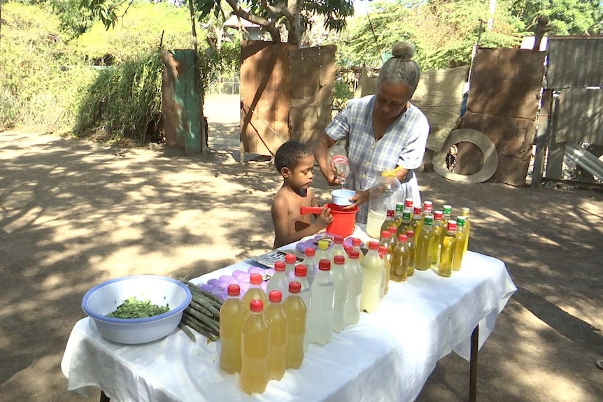 A child holds a bucket for a woman pouring liquid into it.