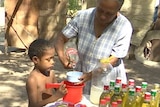A child holds a bucket for a woman pouring liquid into it.