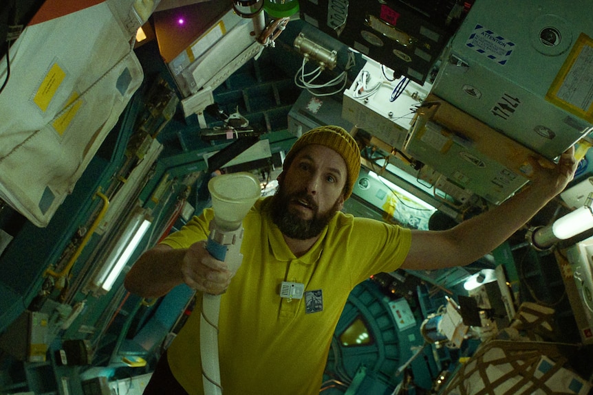 A film still showing a middle-aged white man wearing a beanie holding a torch in a spacecraft 