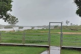 View of a swollen river following heavy rain, with a fence and gate in the foreground