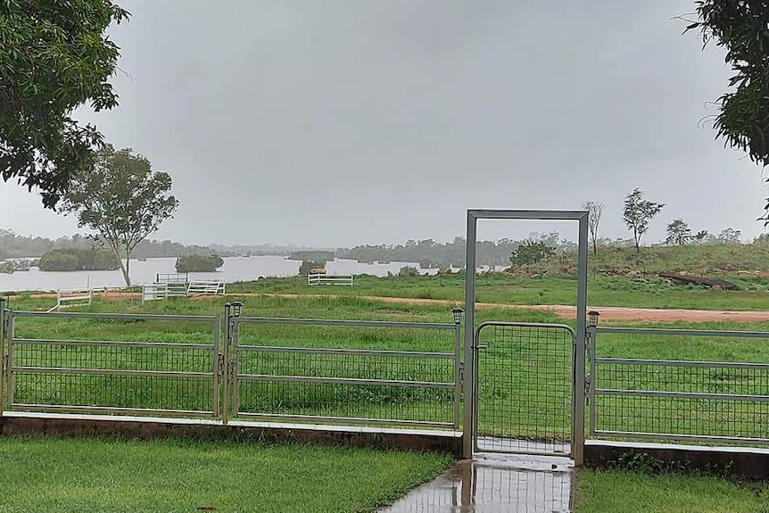 View of a swollen river following heavy rain, with a fence and gate in the foreground