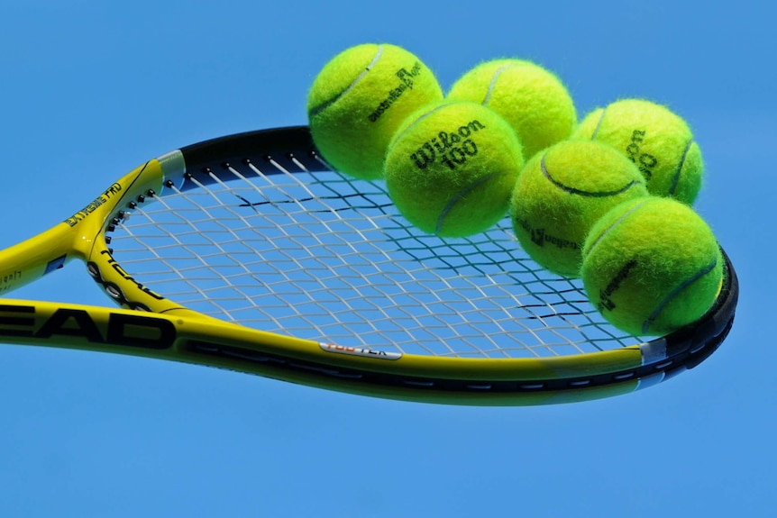 A tennis racquet with several tennis balls balancing on its strings