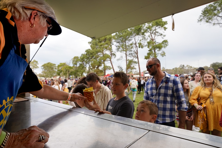 A Millicent Rotary Club volunteer serves a bucket of hot chips to a young customer.