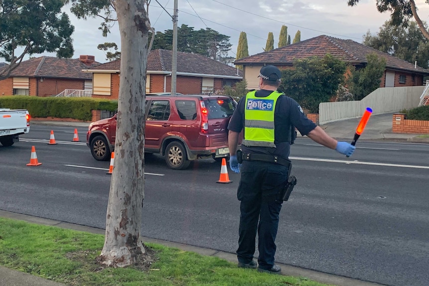 A police officers stop waves cars through a traffic stop.