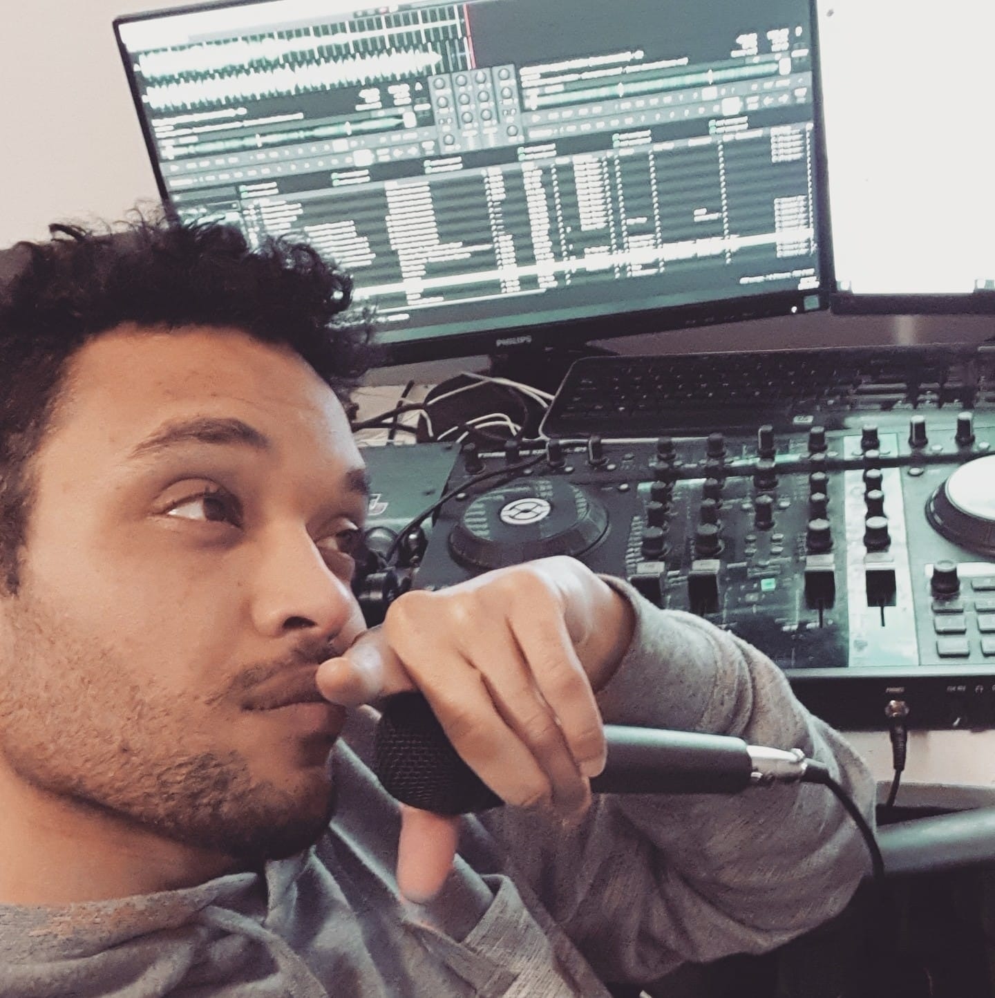 Man sits in front of computer and mixing board with microphone in left hand.