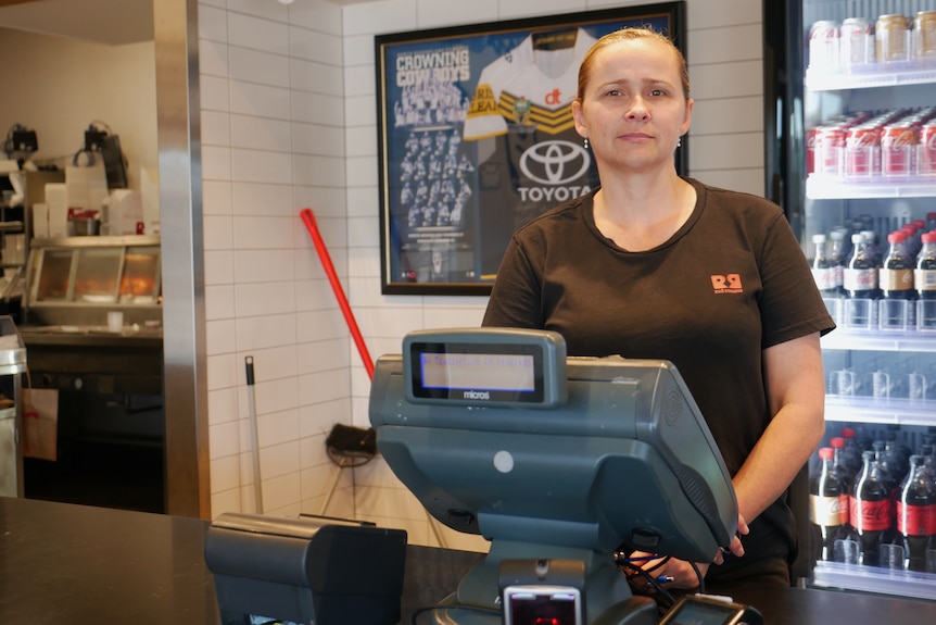 Woman stands behind cash register at fast food restaurant.
