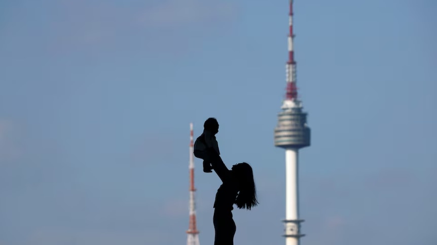 A woman holding up her baby is silhouetted against the backdrop of a tower