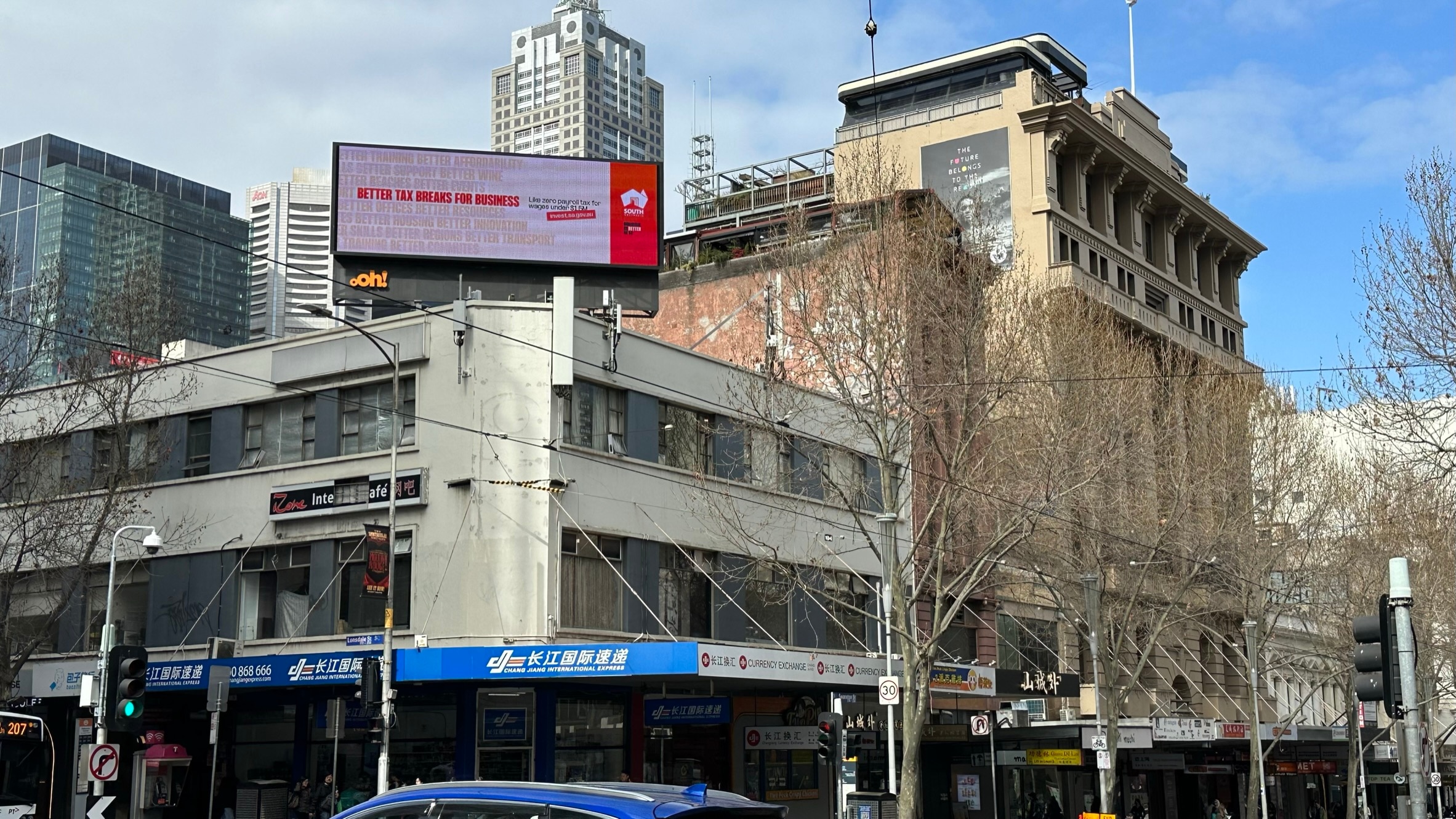A red and white billboard on the top of a building on a street corner in Melbourne to promote doing business in South Australia.