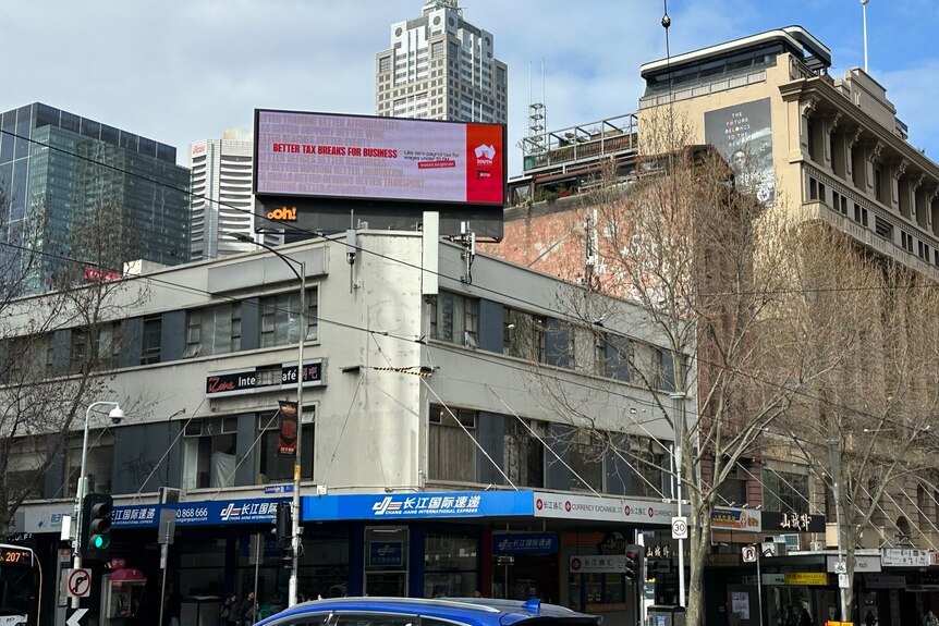 A red and white billboard on the top of a building on a street corner