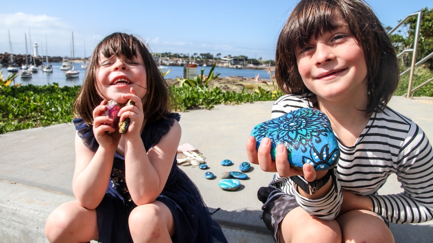Two children show the painted rocks they have found.