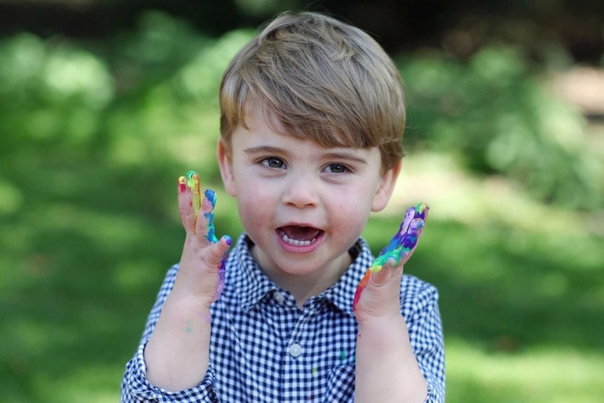 Le prince Louis est représenté avec un immense sourire et les mains couvertes de peinture.