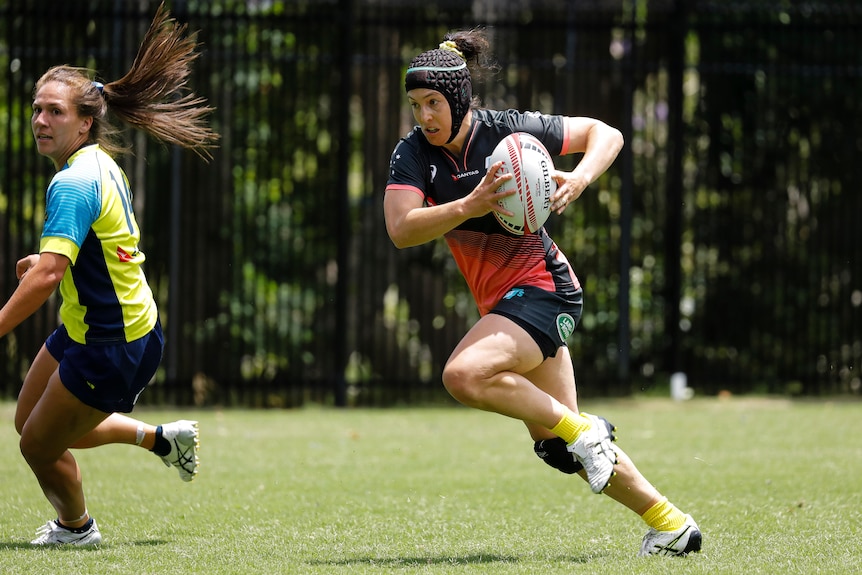 Emilee Cherry runs with a rugby ball by her side being held in both her hands.